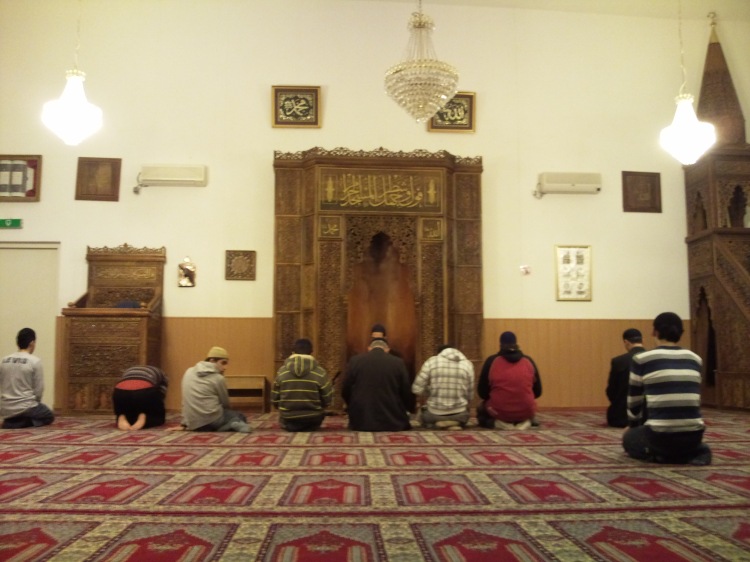 Muslim praying in the masjid while facing the mihrab.